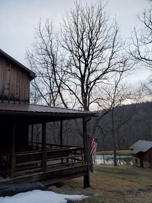 Photo of a corner of Jon's hunting camp from outside. Snow is melting and an American flag can be seen hanging off the porch 